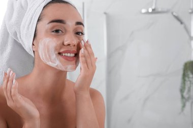 Güzel genç bir kadın banyodaki yüzüne temizleyici köpük sürüyor, mesaj için yer var. Cilt bakımı kozmetik