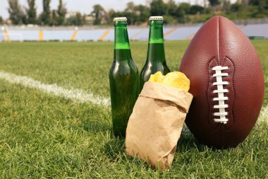 Stadyumdaki yeşil çimlerin üzerinde bira ve patates kızartması olan Amerikan futbol topu. Metin için boşluk
