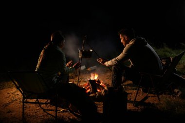 Geceleri kamp ateşinin yanında oturan bir çift.