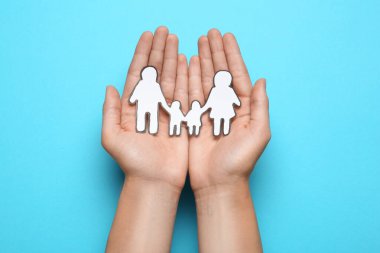 Elinde kağıt aile kesimi olan bir kadın açık mavi arka planda, üst tarafta.