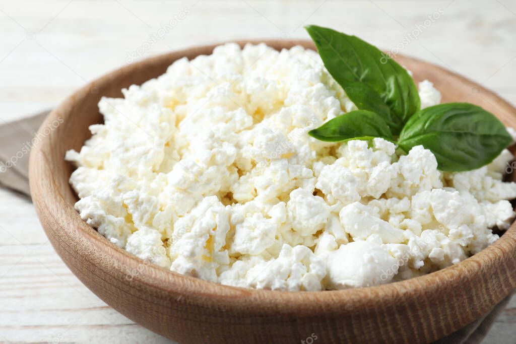 Delicious cottage cheese with basil in wooden bowl on white table, closeup