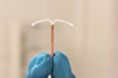Doktor uterus içi doğum kontrol cihazını arka planda tutuyor. Yakın plan.