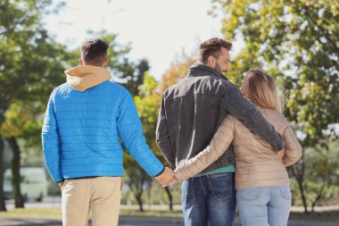 Parkta yürürken erkek arkadaşının arkasından el ele tutuşan bir kadın. Aşk üçgeni