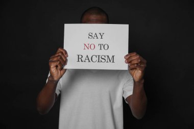 Siyah arka planda ırkçılığa hayır deyin tabelasını tutan Afrikalı Amerikalı bir adam.