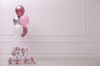 Beyaz duvarın yanında bir sürü hediye kutusu ve balon var. Metin için boşluk