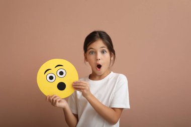 Soluk pembe arka planda şok olmuş emojisi olan duygusal küçük bir kız.