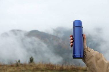Dağlarda elinde mavi termos tutan bir kadın, yakın plan. Metin için boşluk