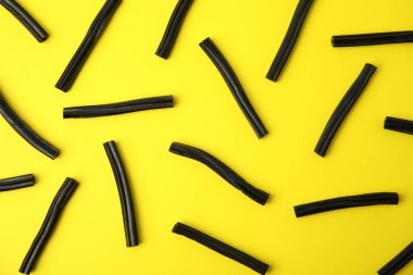 Sarı arka planda siyah meyan kökü şekeri, düz uzanmış.