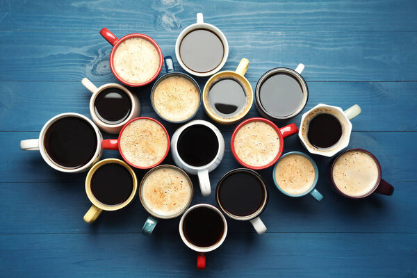 Many cups of different coffee drinks on blue wooden table, flat lay