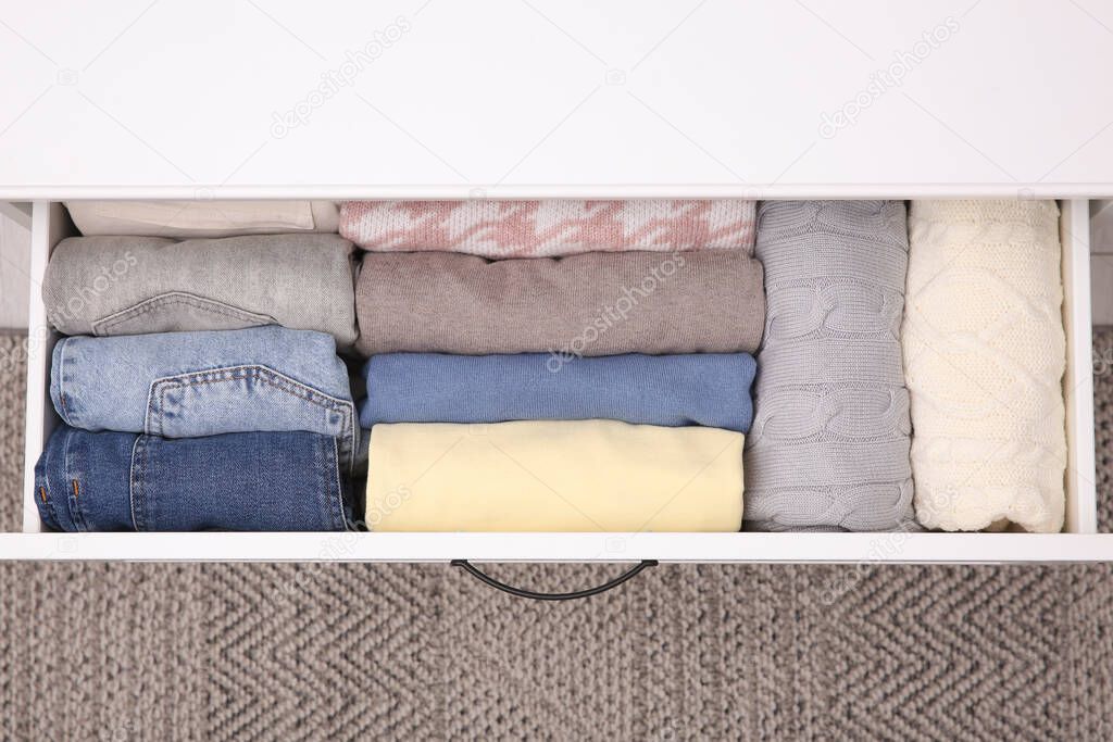 Open drawer with folded clothes indoors, top view. Vertical storage