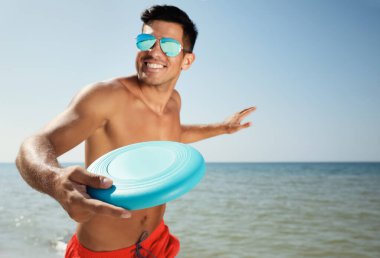 Mutlu adam güneşli bir günde plaja uçan disk atıyor.