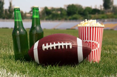 Stadyumdaki yeşil çimlerde bira ve patlamış mısırlı Amerikan futbol topu.