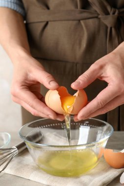 Hafif ahşap masada yumurta sarısını beyazdan ayıran kadın, yakın plan.