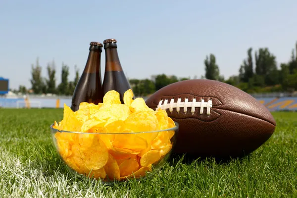 スタジアムの緑の芝生の上にビールとチップを持つアメリカンフットボールボール — ストック写真