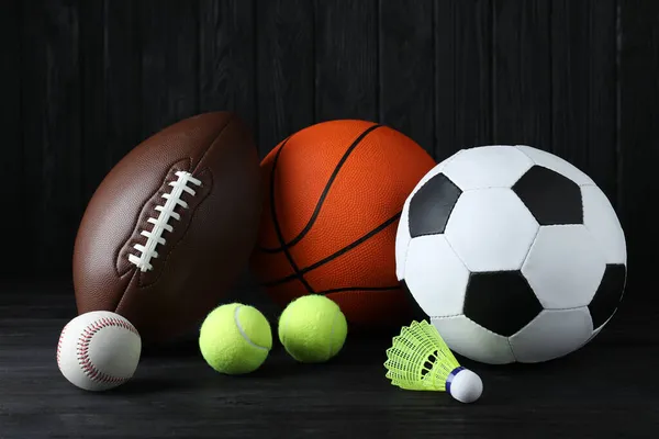 黒い木製のテーブルの上に異なるスポーツボールとシャトルトックのセット — ストック写真