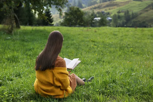 年轻女子在绿草场看书 — 图库照片