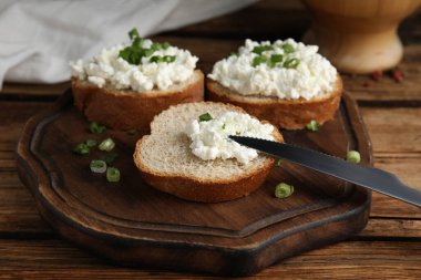 Süzme peynirli ekmek ve ahşap masada yeşil soğan, yakın plan.