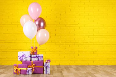 Sarı tuğla duvarın yanında bir sürü hediye kutusu ve balon var. Metin için boşluk
