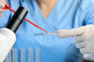 Bilimadamları laboratuardaki mikroskoba kırmızı sıvı damlatıyor.