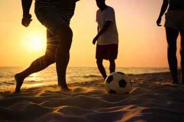 Arkadaşlar gün batımında plajda futbol oynuyor, yakın plan.