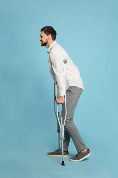 光の青の背景に松葉杖を持つ男の完全な長さの肖像画 — ストック写真