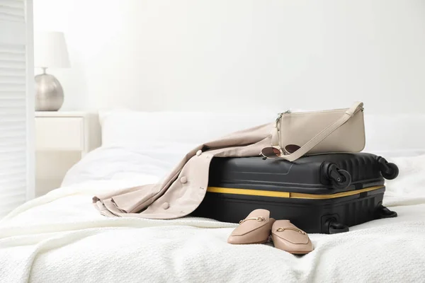 Suitcase packed for trip, shoes, jacket and fashionable accessories on bed in room