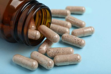 Açık mavi arka planda jelatin kapsüller ve şişe, yakın plan.