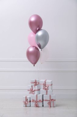 Beyaz duvarın yanında bir sürü hediye kutusu ve balon var.