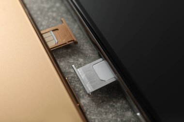 Gri masadaki tepsilerde Sim kartları olan cep telefonları, yakın plan.