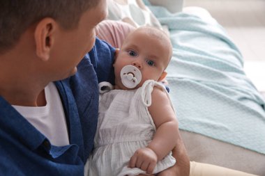 Babası küçük bebeğini kucağında emzik ile evde tutuyor.