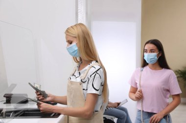 Bankanın vitrininde para sayan koruyucu maskeli bir kadın. Para birimi değişimi