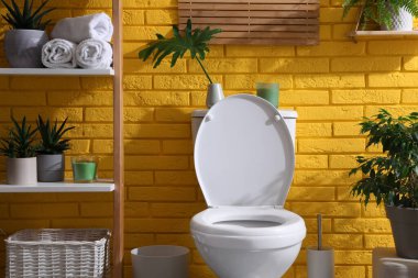 Stylish bathroom with toilet bowl and green plants near yellow brick wall. Interior design clipart
