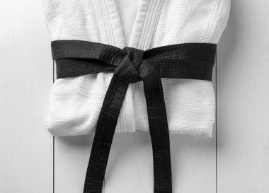 Martial arts uniform with black belt on white wooden background, top view clipart