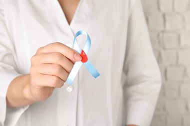 Doktor elinde kağıt kan damlasıyla açık mavi kurdele tutuyor, yakın plan. Dünya Diyabet Günü