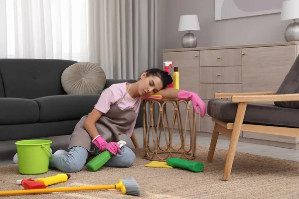 疲惫的年轻女人坐在地板上 在客厅里清洁用品 — 图库照片