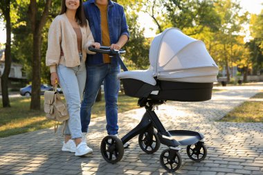 Güneşli bir günde, bebek arabasıyla parkta yürüyen ebeveynler, yakın plan.