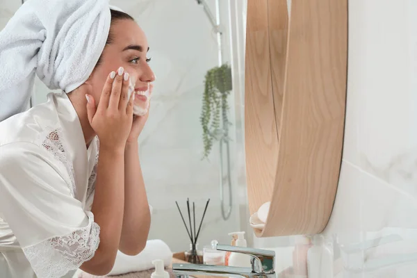 漂亮的年轻女子在浴室靠近镜子的地方涂上清洁剂泡沫 留有文字空间 护肤化妆品 — 图库照片