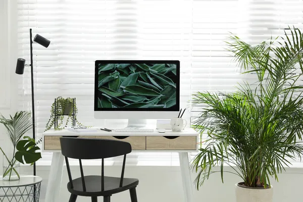 Comfortable workplace with modern computer and green plants in room. Interior design