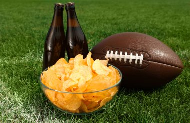 Yeşil çimlerin üzerinde bira ve patates kızartması olan Amerikan futbol topu.