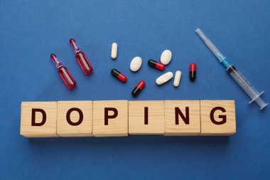 Ahşap küplerde kelime Doping ve uyuşturucu mavi arka planda, düz yatıyordu