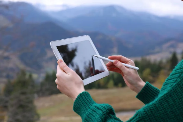 Young woman drawing on tablet in mountains, closeup