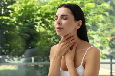 Pencerenin yanında tiroit muayenesi yapan genç bir kadın. Metin için boşluk