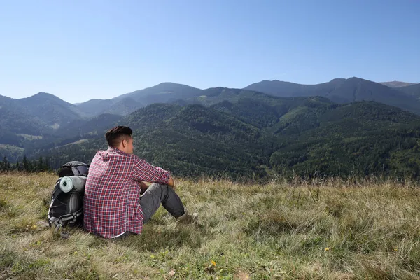 バックパックを地面に座って山の中で風景を楽しむ観光客 バックビュー — ストック写真