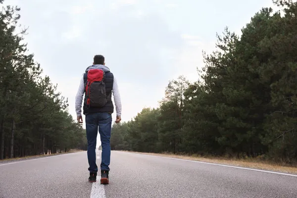 バックパックを持つ男は森の近くの道路に沿って行くバックパックビュー — ストック写真