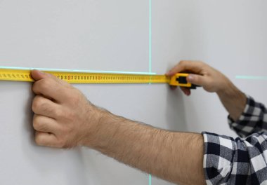 Işık duvarındaki doğru ölçüm için lazer seviyesi ve bant kullanan adam, yakın plan.
