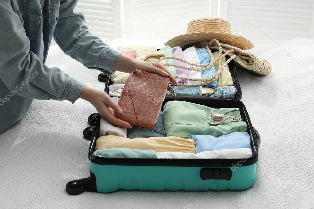 Woman packing suitcase for trip on bed, closeup