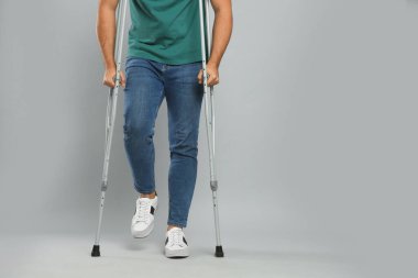 Aksiller koltuk değnekli genç adam gri arka planda, yakın plan. Metin için boşluk