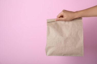Pembe arka planda kese kağıdı tutan kadın, yakın plan. Metin için boşluk