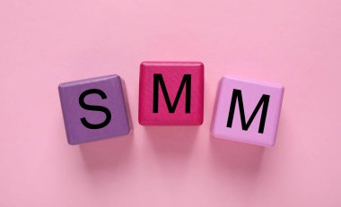 Pembe arka plan üzerinde SMM (Sosyal medya pazarlaması) kısaltması olan renkli küpler, düz konum