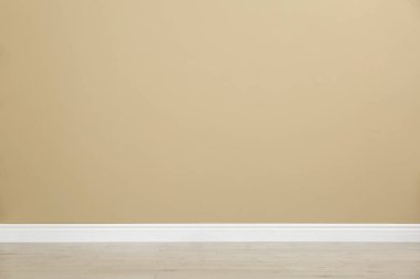 Boş oda, bej duvar ve ahşap zemin.